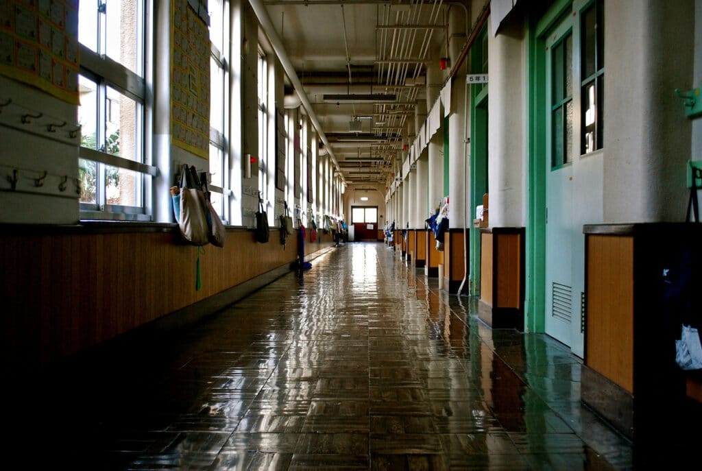 Image of a long school corridor with bags hung up on pegs.